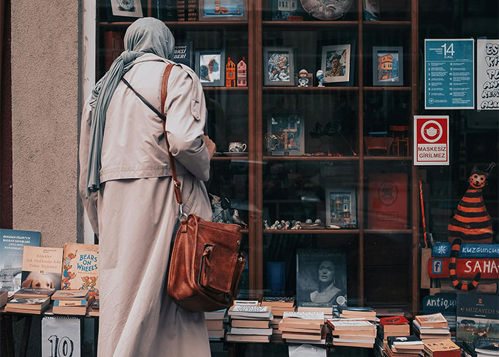 Woman in a long coat and headscarf browsing books, illustrating common adult problems and challenges faced in life.