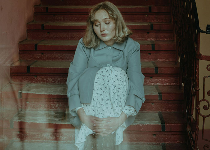 Young woman sitting on stairs looking pensive, illustrating common adult problems many wish they were warned about earlier in life.