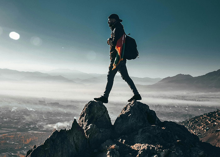 Person standing on rocky peak overlooking foggy landscape symbolizing adult problems and challenges in life journey.