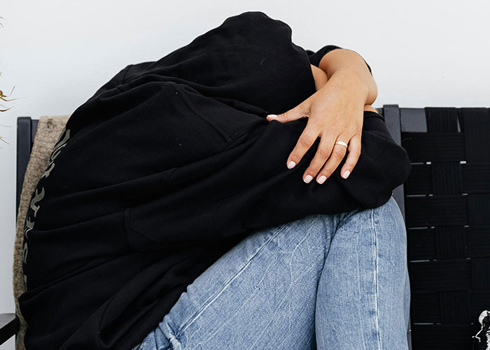 Person in black hoodie sitting curled up on a chair, illustrating adult problems people face in life.
