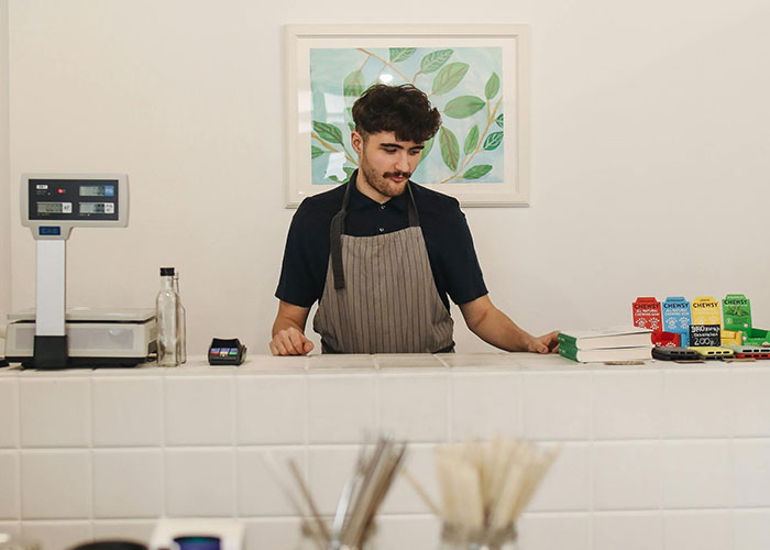 A young man wearing an apron working behind a counter, representing common adult problems in daily life.