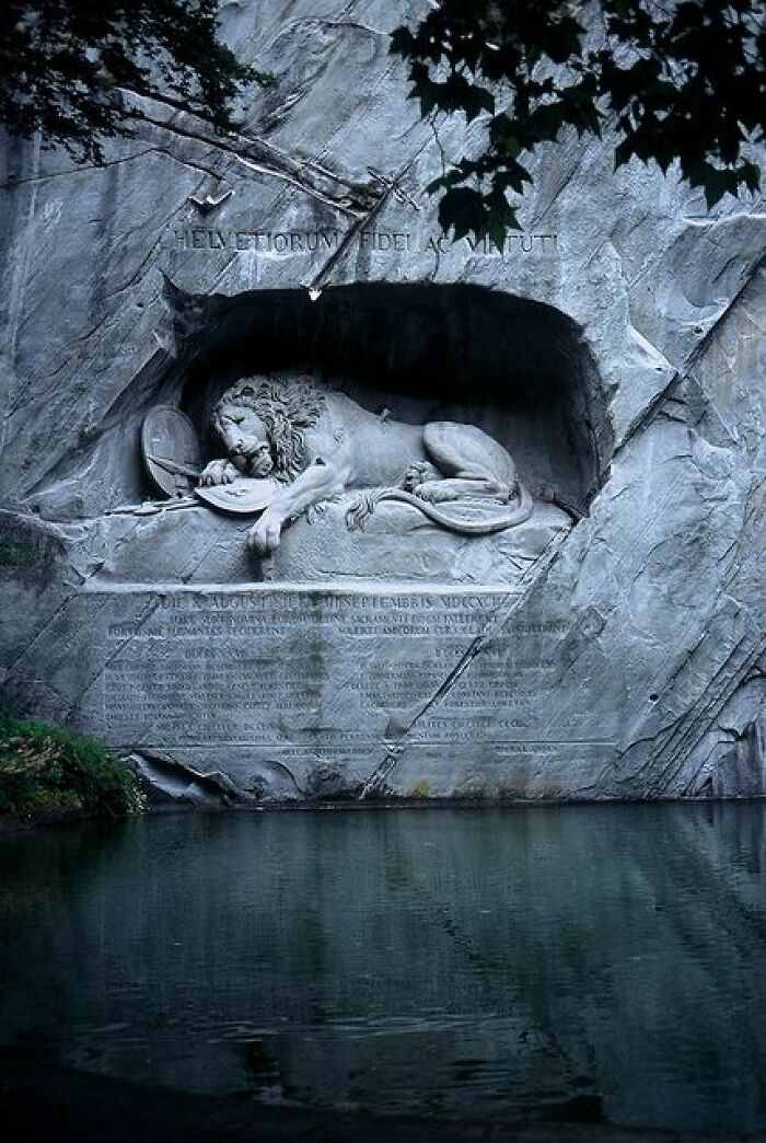 Lion monument carved into rock, reflecting in water, showcasing ancient marvels of craftsmanship.