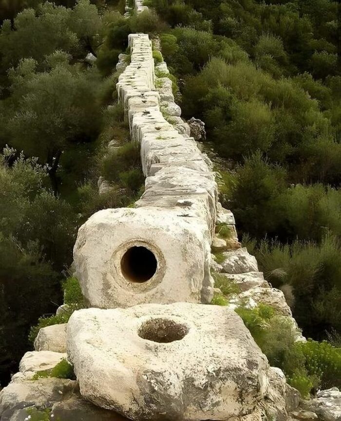 Ancient marvels: stone aqueduct stretching through lush greenery, showcasing impressive engineering.