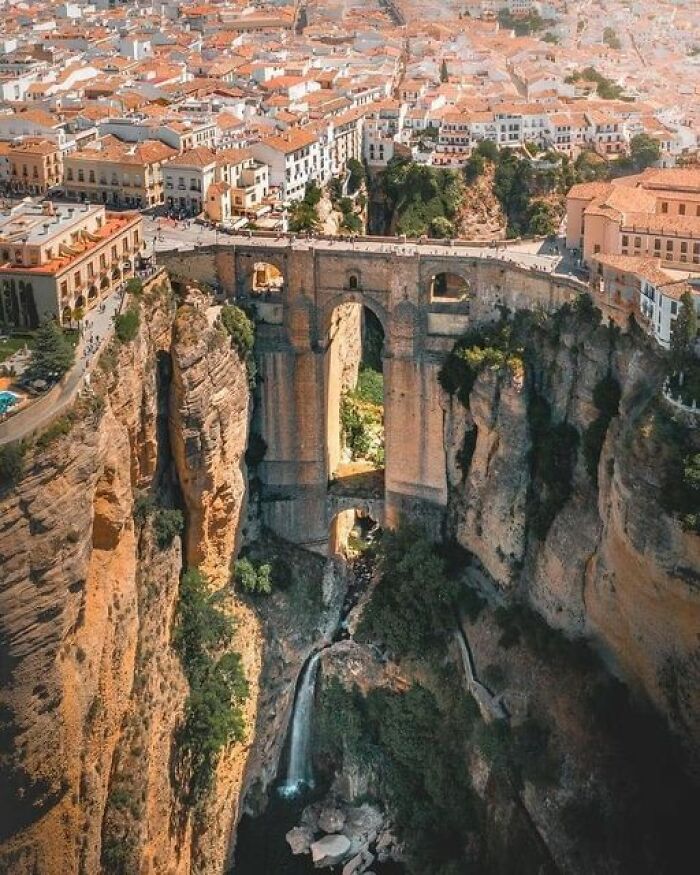 Aerial view of an ancient marvel bridge spanning rugged cliffs with a city backdrop.