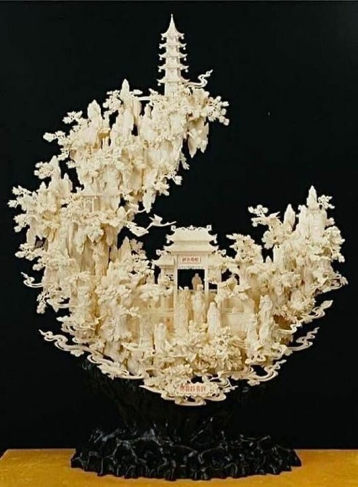 Intricate ivory sculpture resembling ancient marvels with detailed figures and architecture on a dark background.