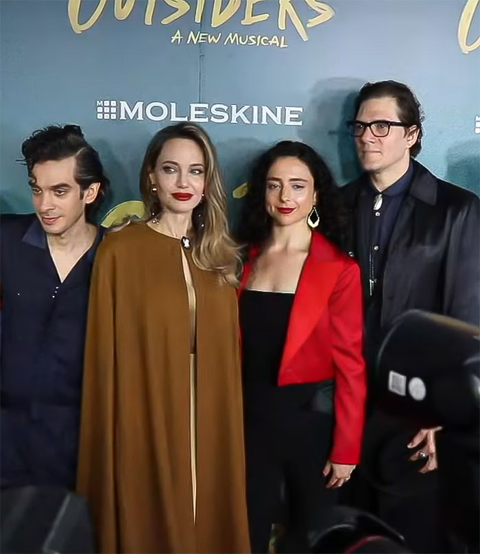 Four people standing together at a red carpet event for "Outsiders: A New Musical," wearing stylish outfits. Four people standing together at a red carpet event for "Outsiders: A New Musical," wearing stylish outfits.