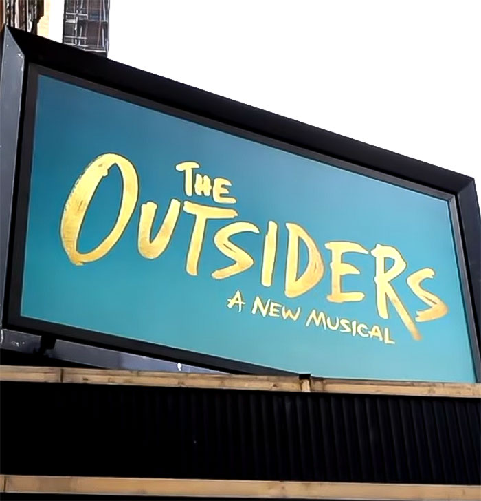 "Billboard for 'The Outsiders' musical, showcasing its title in bold yellow letters on a blue background. "Billboard for 'The Outsiders' musical, showcasing its title in bold yellow letters on a blue background.