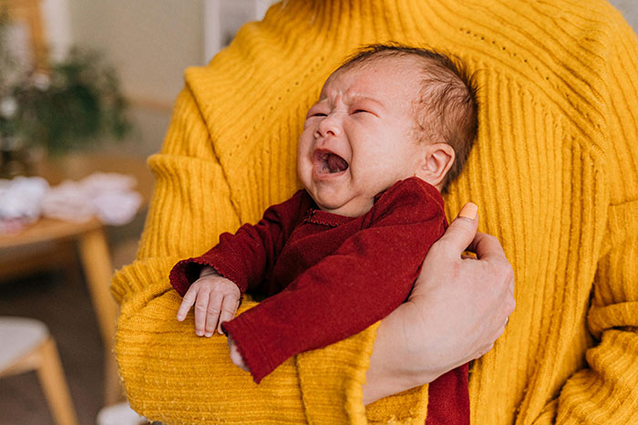 Crying baby held by a person in a yellow sweater, illustrating the impact of the world’s worst parents and CPS cases.