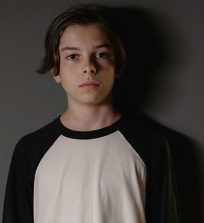 Teenage boy with a serious expression in a black and white shirt, representing impacts of worst parents and CPS intervention.