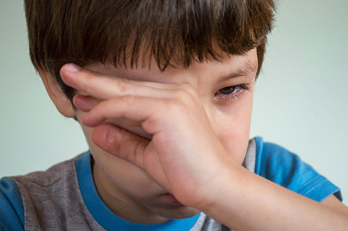 Sad young boy wiping tears from his eyes, illustrating emotional impact of worst parents and child protective services cases.