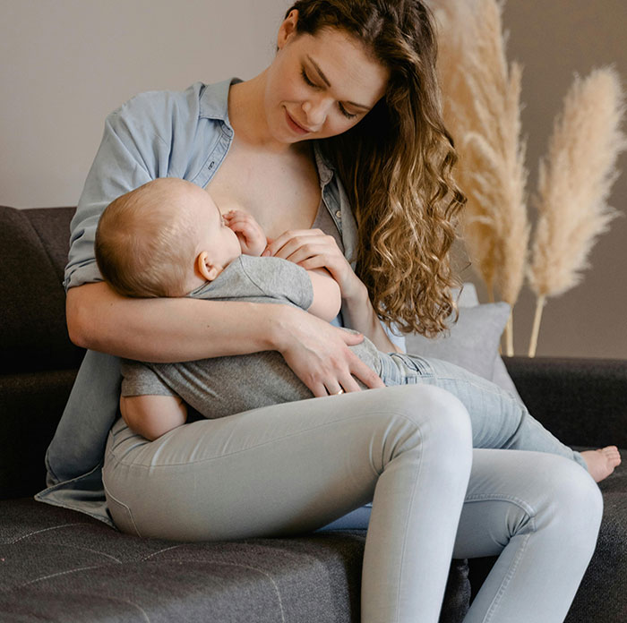 Woman breastfeeding her baby on a couch, representing parenting and child care themes for worst parents stories.