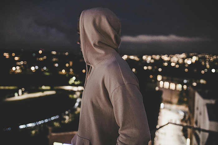 Person wearing a hoodie looking out over a city at night, illustrating themes of encountering the world’s worst parents.