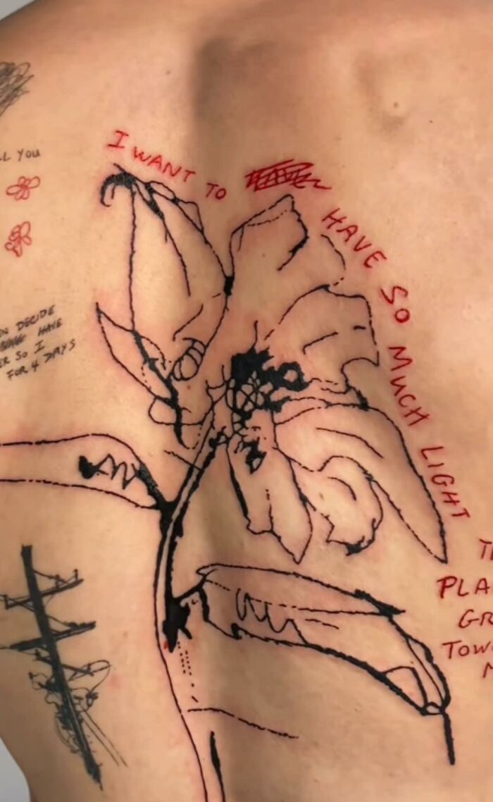 Abstract back tattoo with phrases and a flower, shared in a Facebook group for tattoos that shouldn't exist.