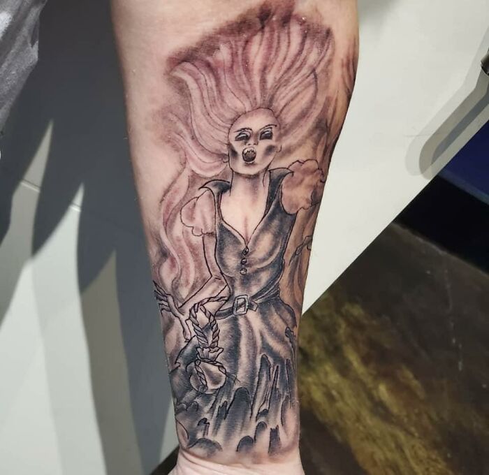 Unusual tattoo of a fantasy figure with flowing hair on an arm, shared by a Facebook group showcasing questionable tattoos.