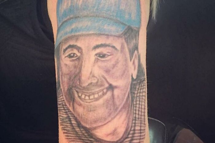Amateurish tattoo depicting a smiling person wearing a blue cap, featured in a Facebook group highlighting questionable tattoos.