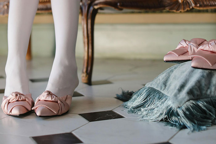 Person wearing pale pink slippers and white stockings standing near matching slippers on a decorative cushion indoors, iconic last words theme.