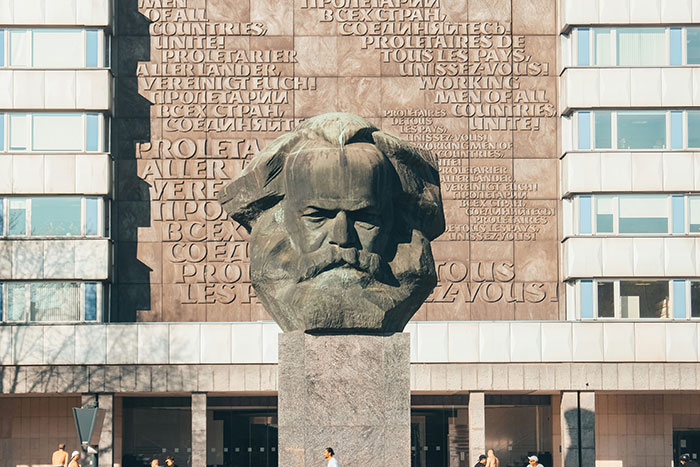 Bust of Karl Marx monument with text in multiple languages on building behind, symbolizing iconic last words in history.