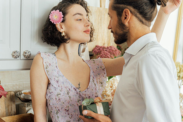 Couple with flowers in a tense moment, possibly falling out of love, in a light-filled kitchen.
