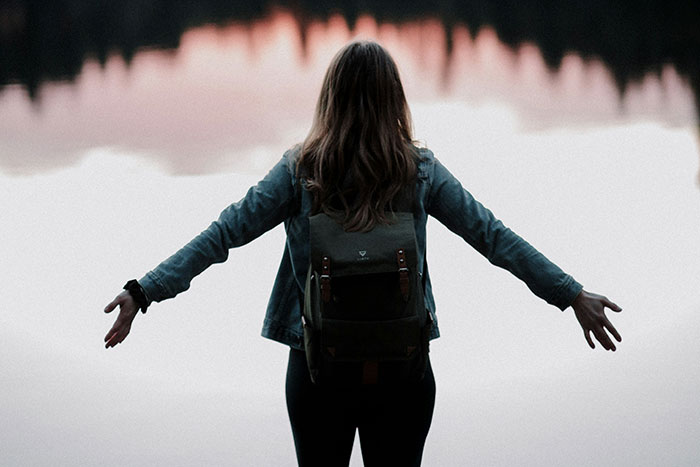 Girl with backpack facing sunset lake; symbolizing falling out of love.