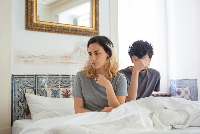 Couple sitting in bed, looking distant and upset, signaling falling out of love.
