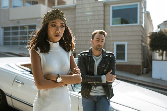 A couple looking distant and stressed beside a car, signaling falling out of love on a sunny street.