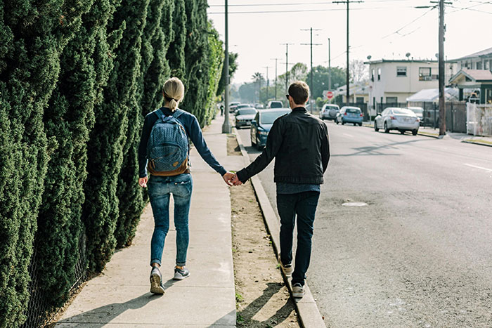 Couple holding hands on a sidewalk, hinting at signs of falling out of love.