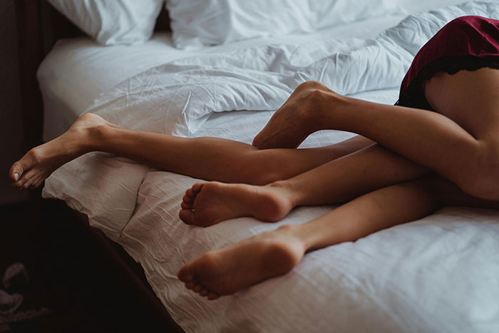 Two people lying closely in bed, legs intertwined, suggesting falling out of love.