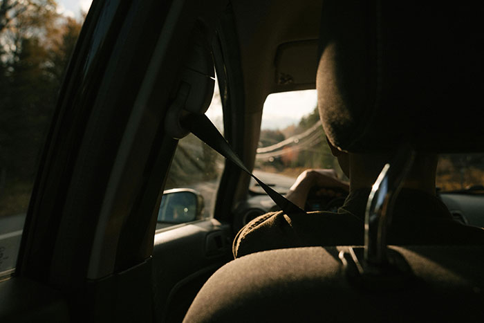 A person sitting in a car, seatbelt fastened, with sunlight streaming through the window, feeling disconnected.