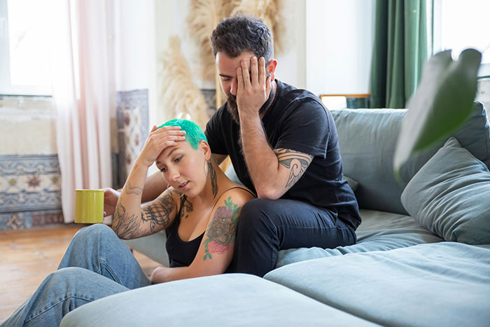 A couple sitting apart on a couch, looking distressed, signaling falling out of love.