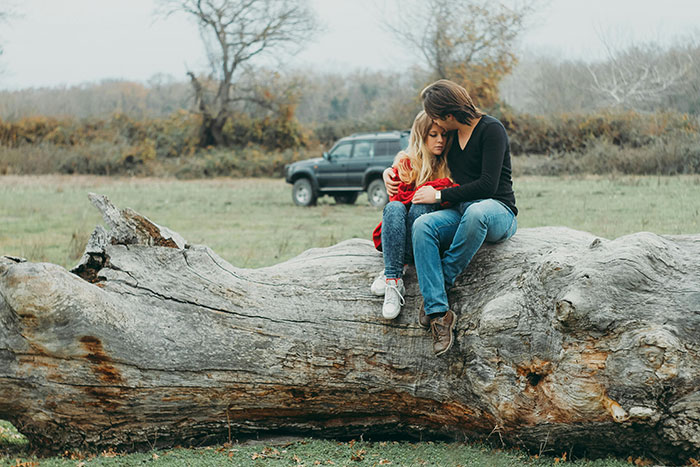 Two people sit silently on a fallen tree in a field, indicating falling out of love.