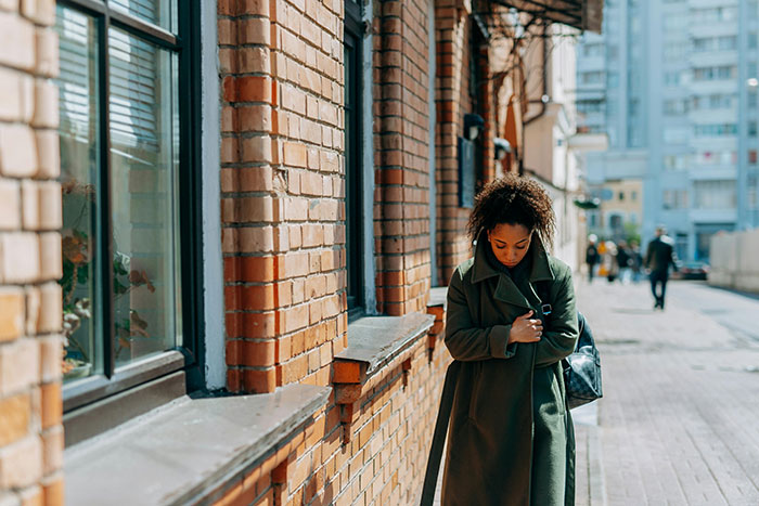 Woman walking on a city street, wearing a green coat, seemingly lost in thought, illustrating falling out of love.