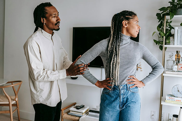 Man and woman in tense discussion, signaling falling out of love, in living room with plants and wall decor.