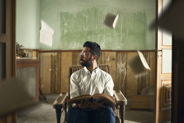 A man in a chair surrounded by flying books.