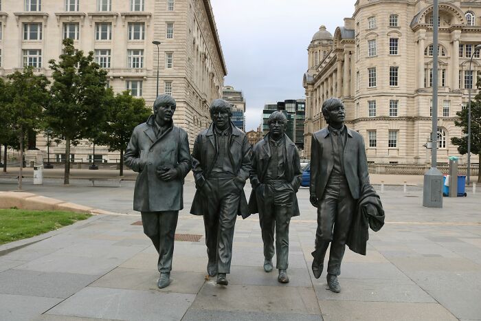 Statues of four men in coats walking in a city plaza.