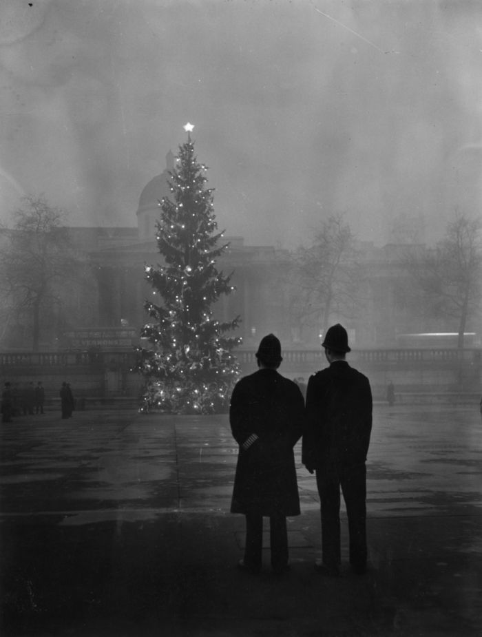 Vintage photo of two policemen standing in front of a decorated Christmas tree in a foggy city square from a historical photo group.