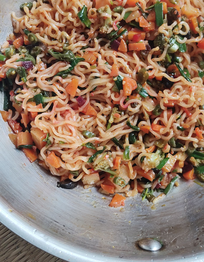 A colorful lunch idea featuring stir-fried noodles mixed with chopped vegetables, including carrots, green onions, and peas, served in a silver pan. A colorful lunch idea featuring stir-fried noodles mixed with chopped vegetables, including carrots, green onions, and peas, served in a silver pan.