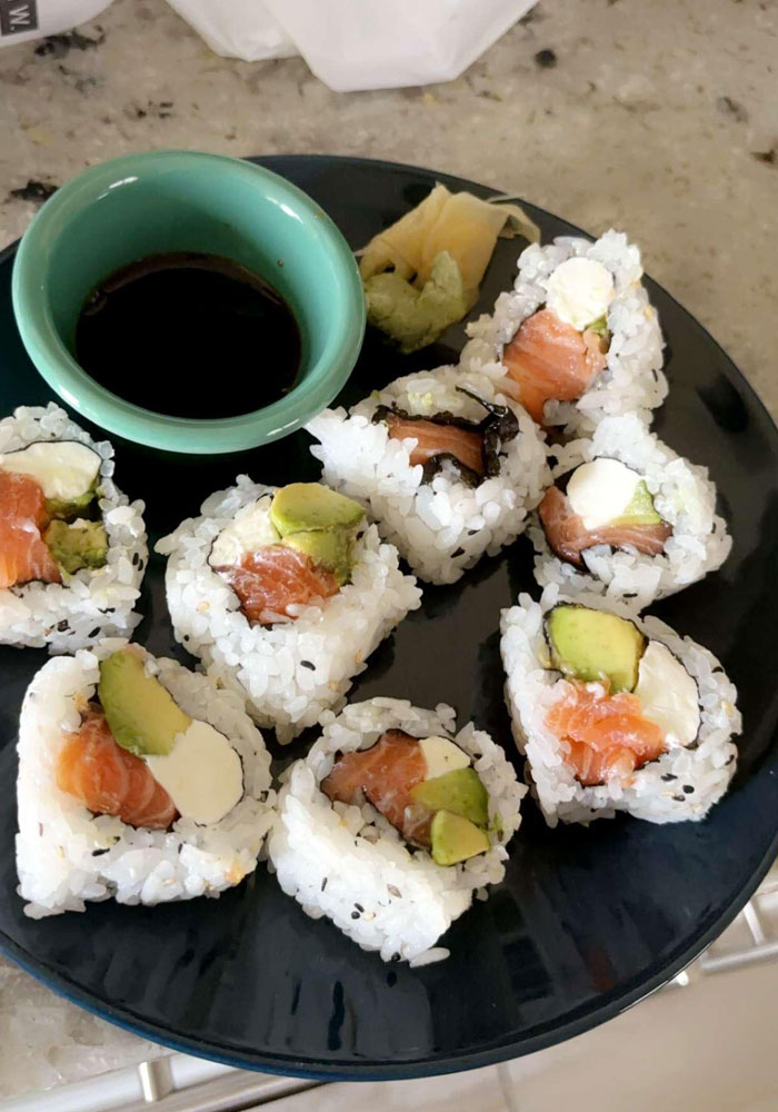 A plate of sushi rolls filled with salmon, avocado, and cream cheese, served with soy sauce, wasabi, and pickled ginger on the side. The dish is arranged on a dark plate with a small dipping bowl of soy sauce. A plate of sushi rolls filled with salmon, avocado, and cream cheese, served with soy sauce, wasabi, and pickled ginger on the side. The dish is arranged on a dark plate with a small dipping bowl of soy sauce.