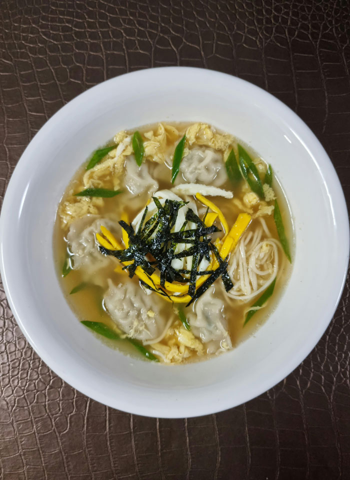 A warm lunch idea featuring a bowl of dumpling soup with noodles, garnished with strips of seaweed, sliced egg, green onions, and enoki mushrooms, served in a light broth. A warm lunch idea featuring a bowl of dumpling soup with noodles, garnished with strips of seaweed, sliced egg, green onions, and enoki mushrooms, served in a light broth.
