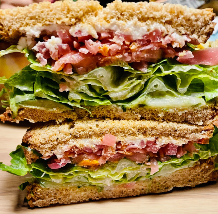 A stacked sandwich filled with layers of fresh lettuce, sliced tomatoes, cucumbers, and creamy spread, served between slices of whole wheat bread. A stacked sandwich filled with layers of fresh lettuce, sliced tomatoes, cucumbers, and creamy spread, served between slices of whole wheat bread.