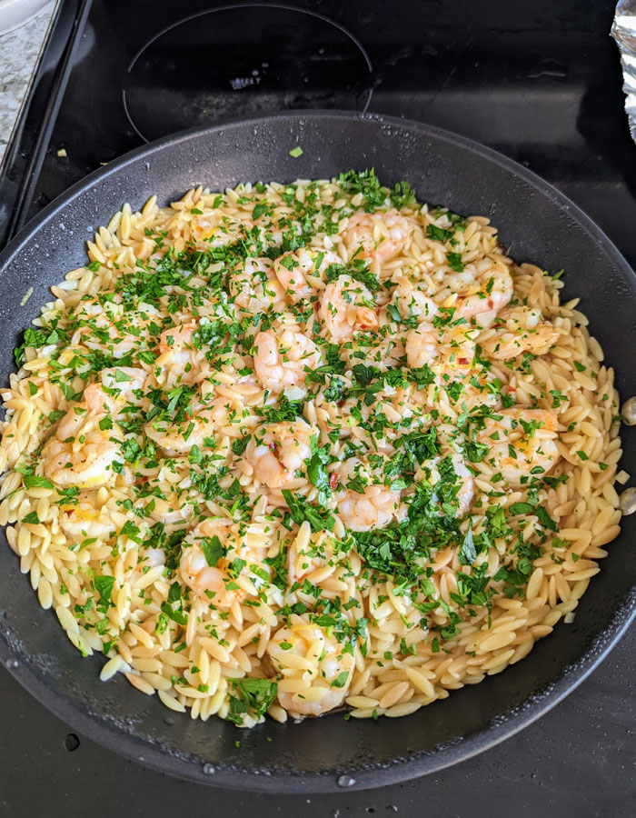 A delicious lunch idea featuring a pan of orzo pasta mixed with shrimp, garnished generously with fresh parsley and a light sauce. A delicious lunch idea featuring a pan of orzo pasta mixed with shrimp, garnished generously with fresh parsley and a light sauce.