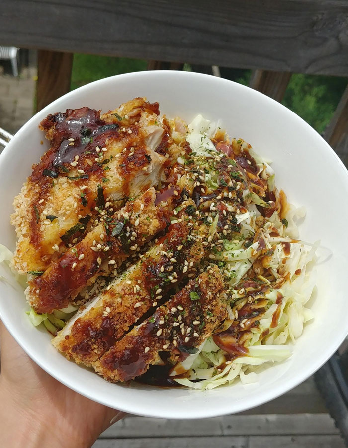 A flavorful lunch idea featuring crispy breaded chicken cutlets drizzled with sauce, served on a bed of shredded cabbage, and garnished with sesame seeds and herbs in a white bowl. A flavorful lunch idea featuring crispy breaded chicken cutlets drizzled with sauce, served on a bed of shredded cabbage, and garnished with sesame seeds and herbs in a white bowl.