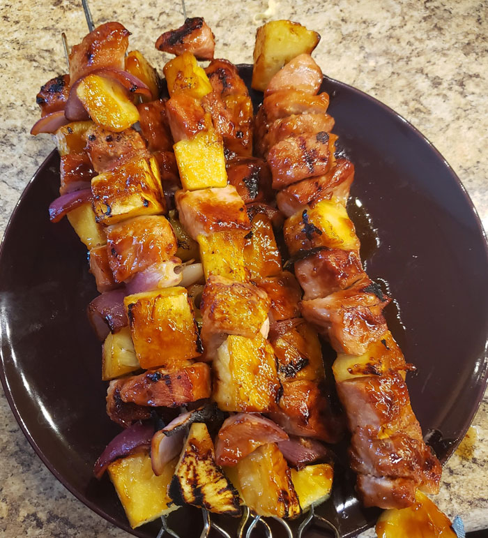 A savory lunch idea featuring grilled skewers of marinated meat, pineapple, and red onions, served on a dark plate with a caramelized glaze. A savory lunch idea featuring grilled skewers of marinated meat, pineapple, and red onions, served on a dark plate with a caramelized glaze.
