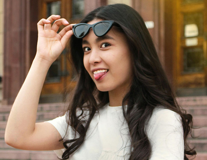 Young woman with long hair playfully lifting sunglasses, showcasing attractive minor things on women outdoors.