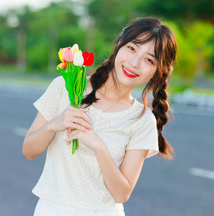 Young woman with braided hair holding colorful tulips, showcasing subtle attractive features women often overlook.