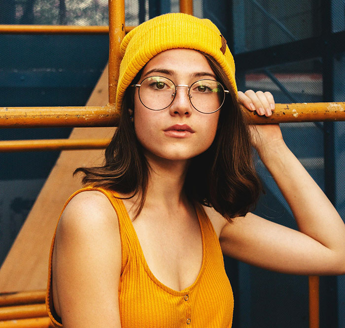 Young woman wearing glasses and a yellow beanie showcasing minor attractive features on women in a casual setting.