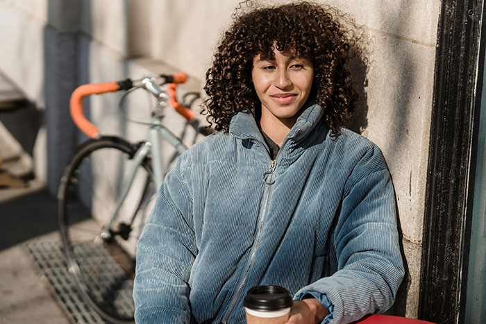 Woman with curly hair and casual jacket smiling outdoors holding coffee, highlighting attractive minor things on women.