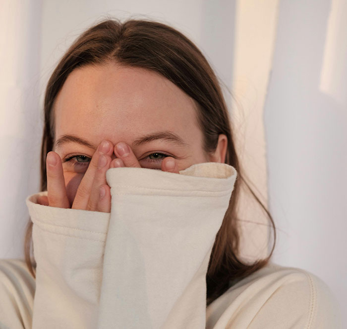 Young woman smiling shyly, covering part of her face with sleeves, highlighting minor attractive features on women.