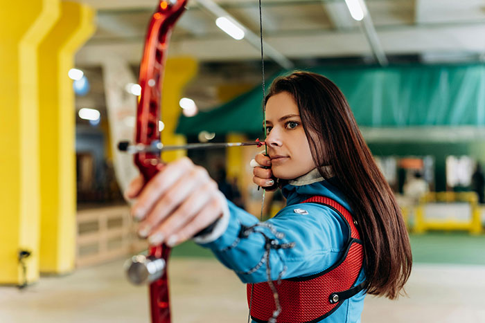 Young woman practicing archery indoors, showing focus and confidence, highlighting attractive minor details on women.