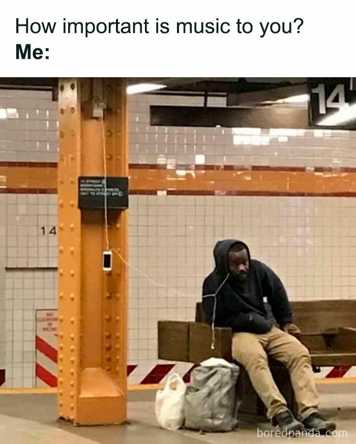 Man listening to music on headphones in a subway, phone charging on a pillar.