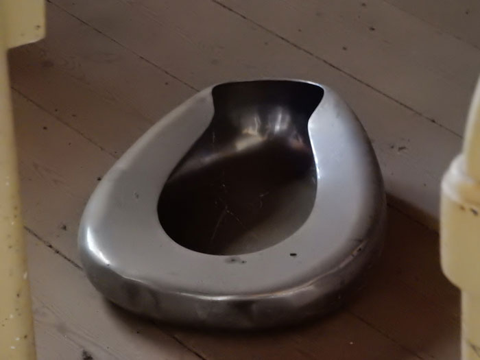 Metal bedpan on wooden floor.
